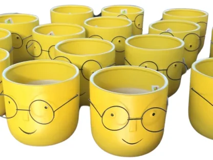 עציץ קרמי צהוב עם ציור פנים ומשקפיים,